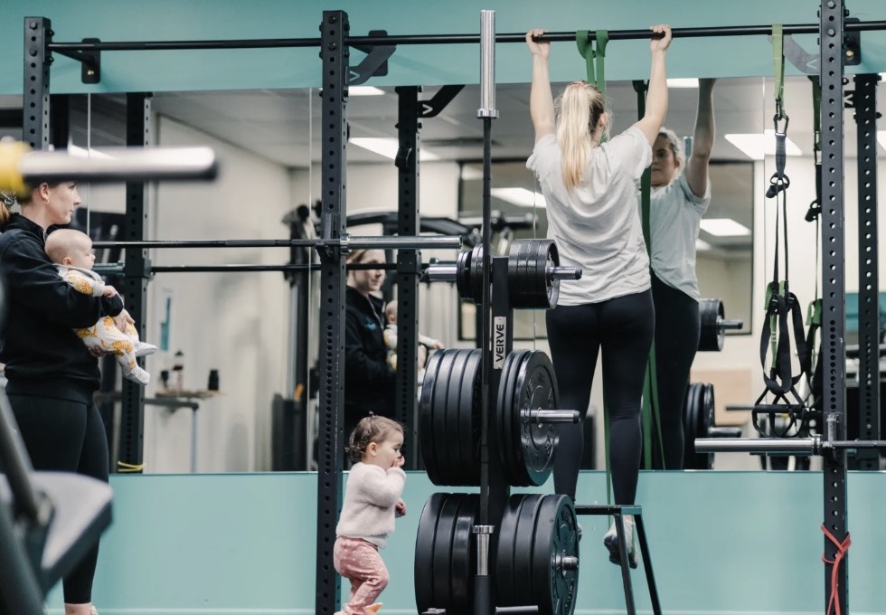 A mum doing pull-ups in a gym with her baby held nearby